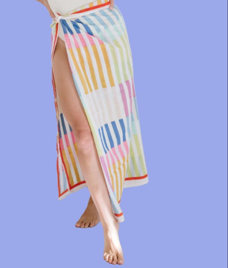 A person wearing a multicolored striped sarong with a geometric pattern, posing against a blue background.