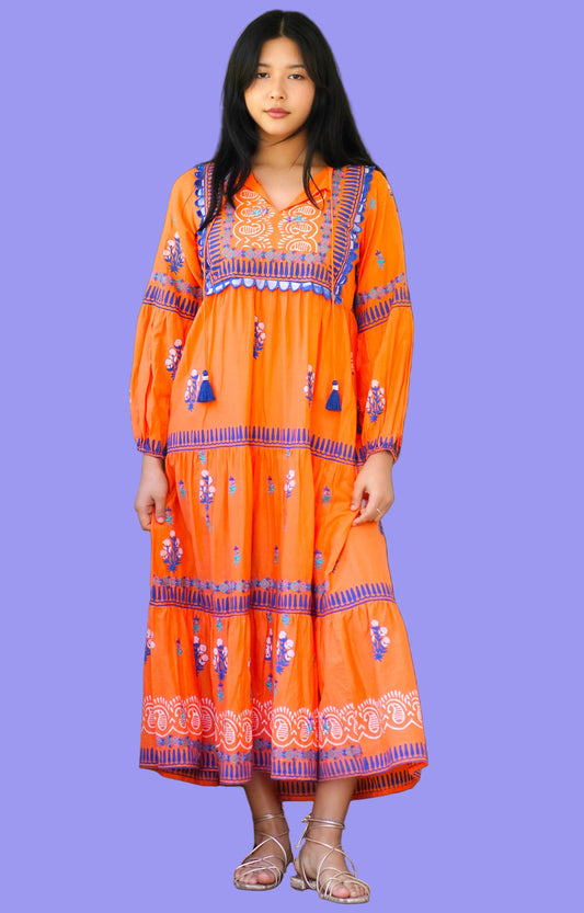 Woman wearing an orange embroidered dress standing in front of a door.