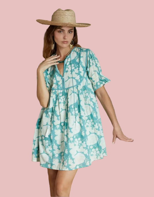 Woman in a floral dress standing in a room with wooden walls and shelves.