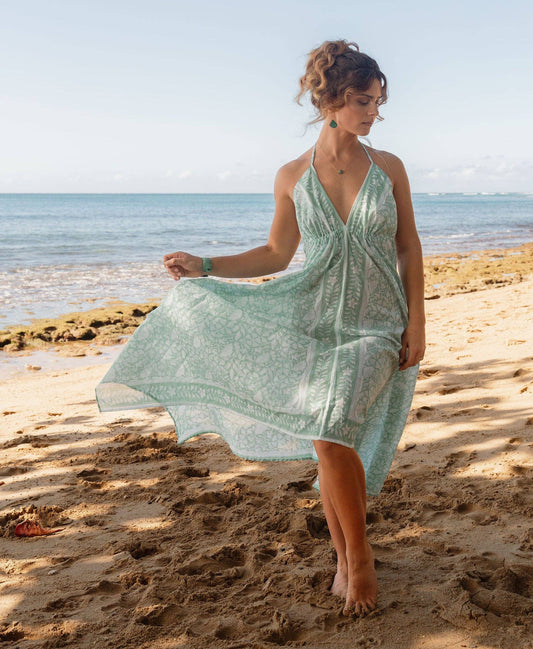 Woman in a light green dress standing on a sandy beach with ocean and sky in the background